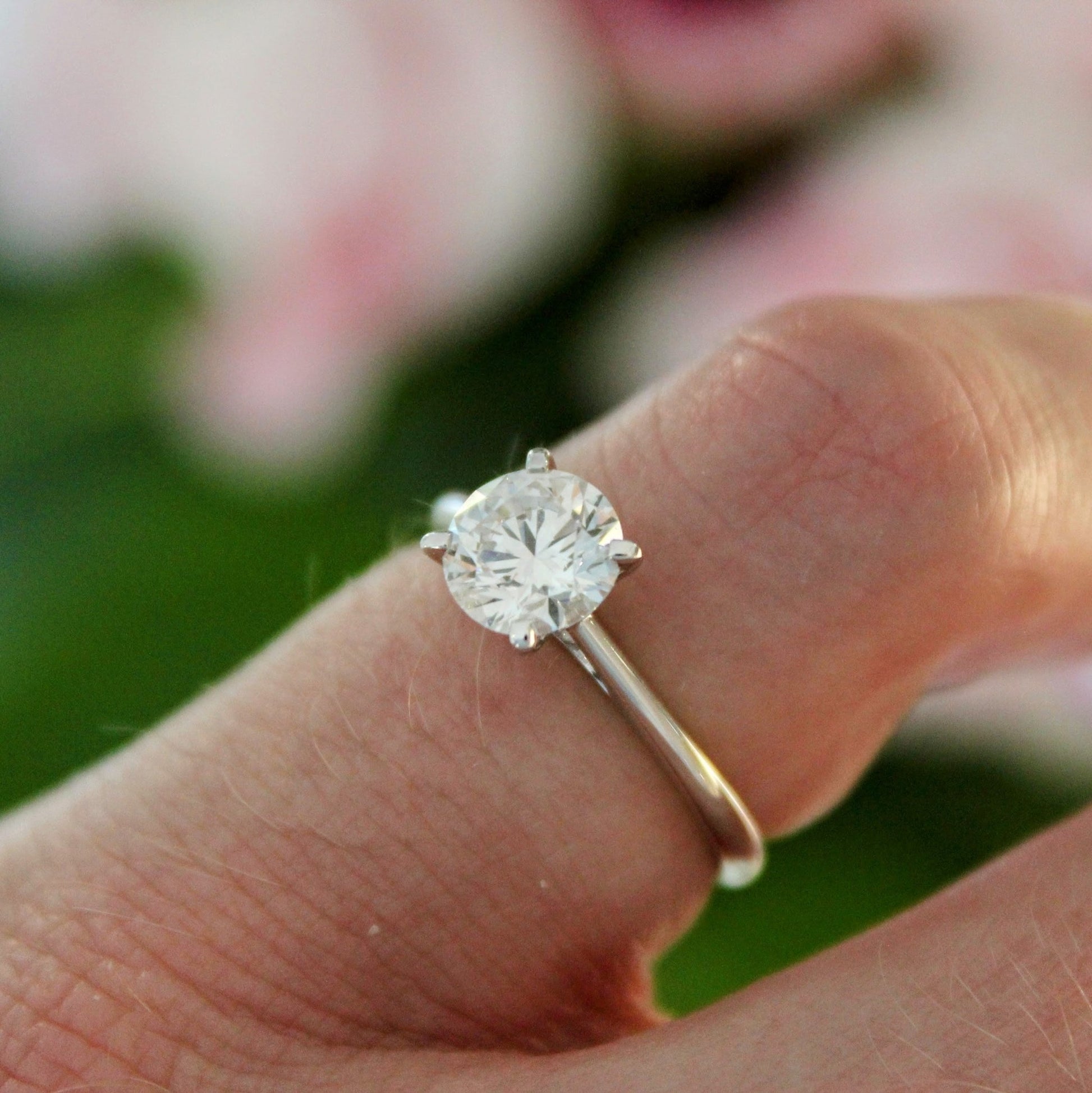 A close-up of a hand wearing a four-prong solitaire engagement ring, featuring a sparkling lab-grown diamond set in 18K white gold.