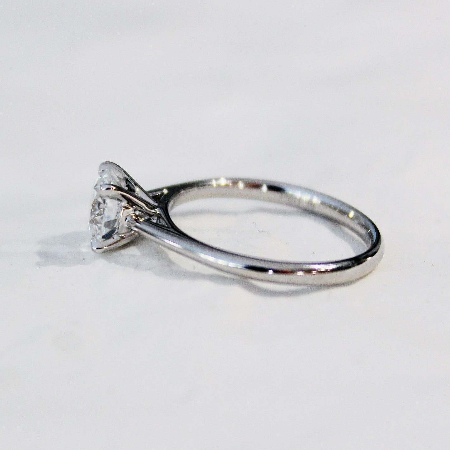 A detailed side view of a four-prong solitaire engagement ring, featuring a lab-grown diamond set in a sleek 18K white gold band, showcased on a white surface.