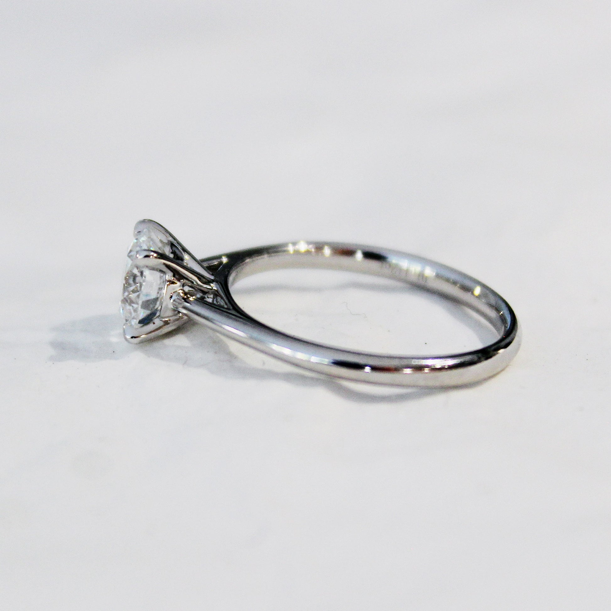A detailed side view of a four-prong solitaire engagement ring, featuring a lab-grown diamond set in a sleek 18K white gold band, showcased on a white surface.