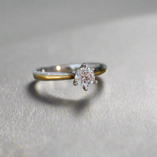 Close-up of a two-tone solitaire diamond engagement ring displayed on a textured surface, featuring an 18K solid gold band and a stunning lab-grown diamond with exceptional brilliance.